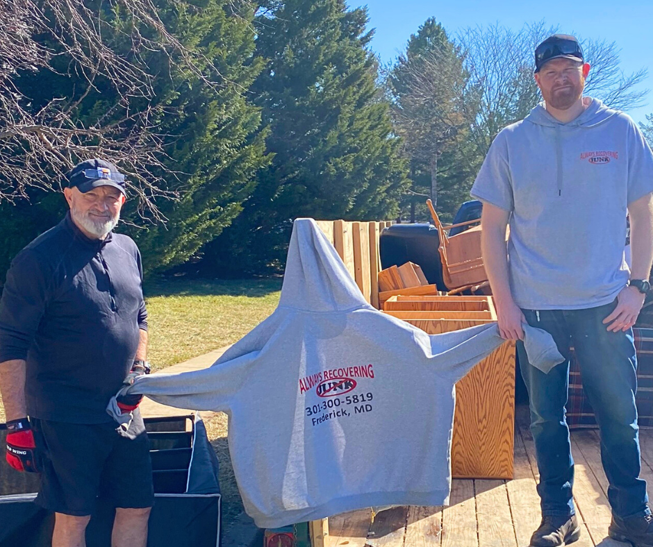 two of our male team members holding an Always Recovering Junk sweatshirt to display our logo during a junk removal frederick md job